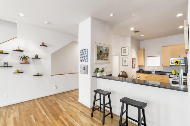kitchen with light brown cabinetry, dark countertops, a breakfast bar area, stainless steel appliances, and visible vents