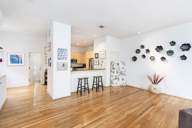 interior space featuring light brown cabinetry, a kitchen breakfast bar, recessed lighting, light wood finished floors, and stainless steel appliances