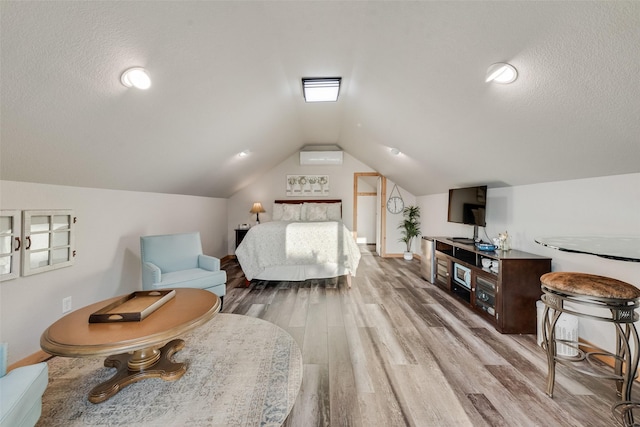 bedroom featuring an AC wall unit, a textured ceiling, baseboards, wood finished floors, and vaulted ceiling