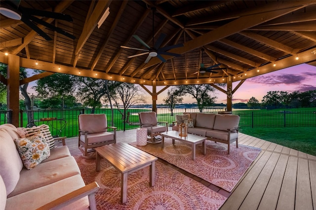 deck at dusk with fence, a gazebo, ceiling fan, outdoor lounge area, and a lawn
