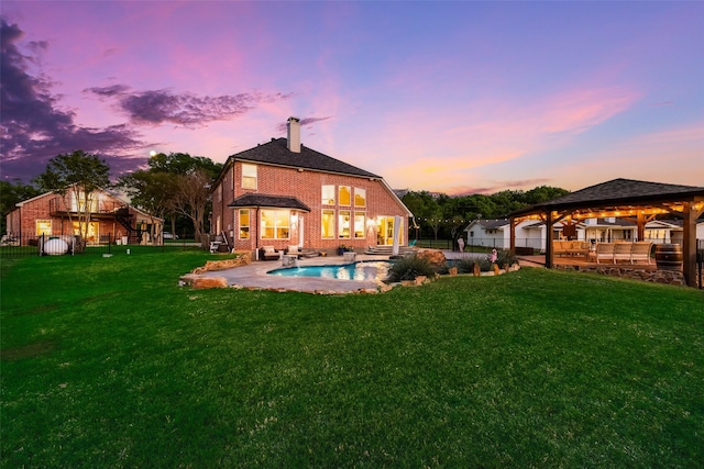 back of property at dusk featuring a chimney, a lawn, fence private yard, brick siding, and a gazebo