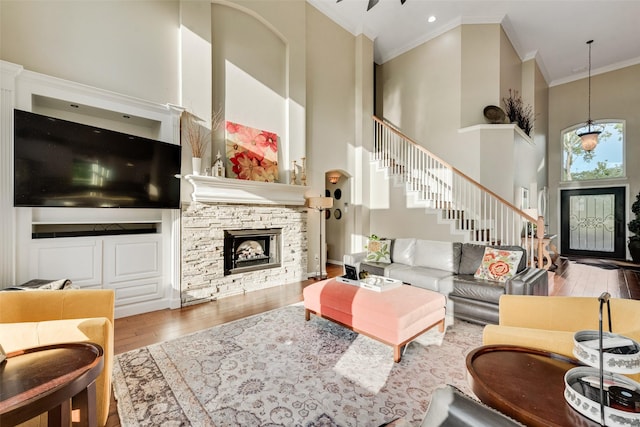 living area featuring crown molding, stairs, a fireplace, hardwood / wood-style floors, and a high ceiling
