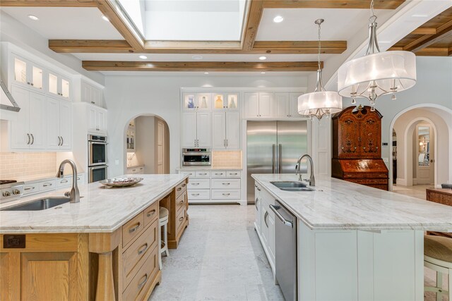 kitchen featuring arched walkways, a large island with sink, a sink, and stainless steel appliances