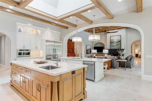 kitchen with a large island, a lit fireplace, arched walkways, a sink, and stainless steel appliances