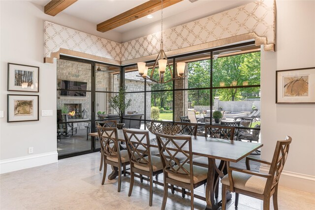dining area featuring baseboards, a warm lit fireplace, a chandelier, and beamed ceiling