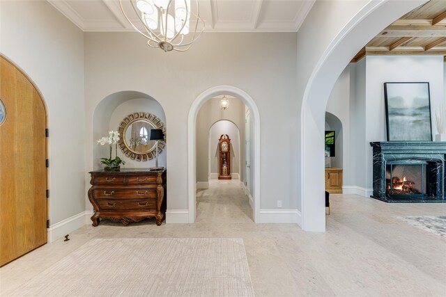 foyer featuring crown molding, arched walkways, a fireplace, baseboards, and a chandelier
