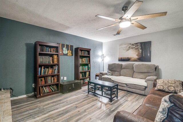 living area with visible vents, a textured wall, wood finished floors, baseboards, and a ceiling fan