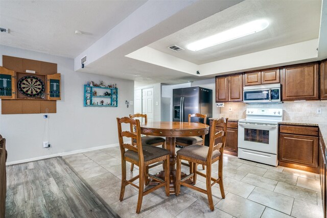 kitchen featuring brown cabinetry, visible vents, tasteful backsplash, light countertops, and stainless steel appliances