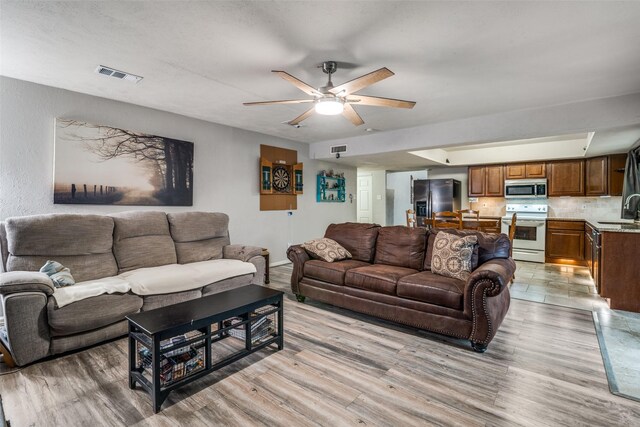 living area featuring a ceiling fan, baseboards, visible vents, and light wood-type flooring