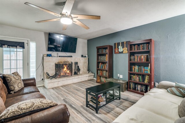 living area with a textured wall, ceiling fan, wood finished floors, and a lit fireplace