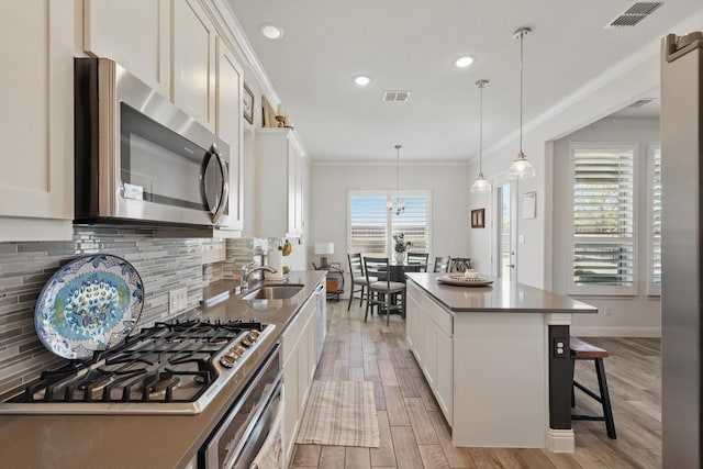 kitchen with a sink, ornamental molding, stainless steel appliances, and visible vents