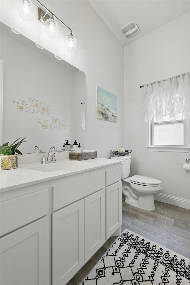bathroom featuring toilet, baseboards, wood finished floors, and vanity