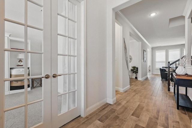 hallway featuring french doors, baseboards, ornamental molding, and wood finished floors
