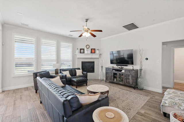 living area with visible vents, a ceiling fan, baseboards, and crown molding