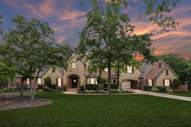 view of front of property featuring a lawn, driveway, stone siding, and a garage