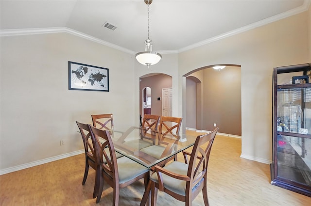 dining room with visible vents, arched walkways, baseboards, ornamental molding, and light wood-style flooring