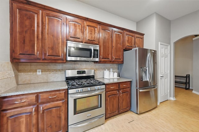 kitchen with stainless steel appliances, arched walkways, decorative backsplash, and light wood-style floors