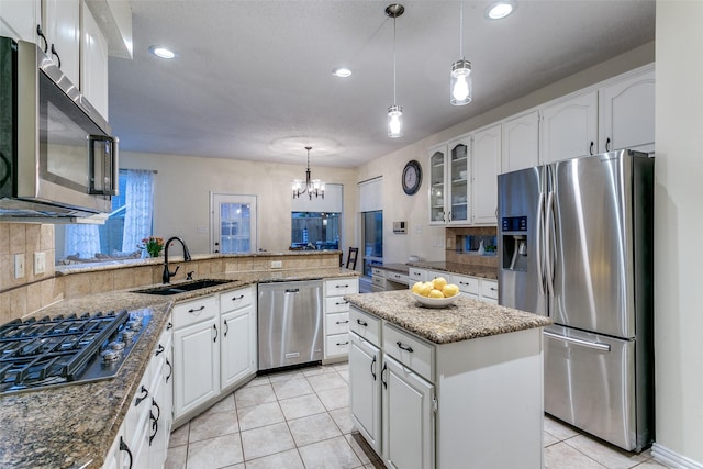 kitchen with appliances with stainless steel finishes, a sink, light tile patterned floors, a chandelier, and glass insert cabinets