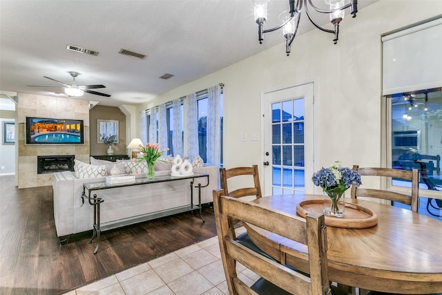 dining area featuring visible vents, a tiled fireplace, wood finished floors, and ceiling fan with notable chandelier