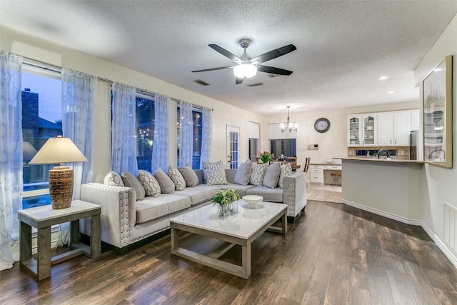 living area with a textured ceiling, visible vents, dark wood finished floors, and ceiling fan with notable chandelier