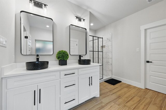 full bathroom with a sink, a shower stall, double vanity, and wood finished floors