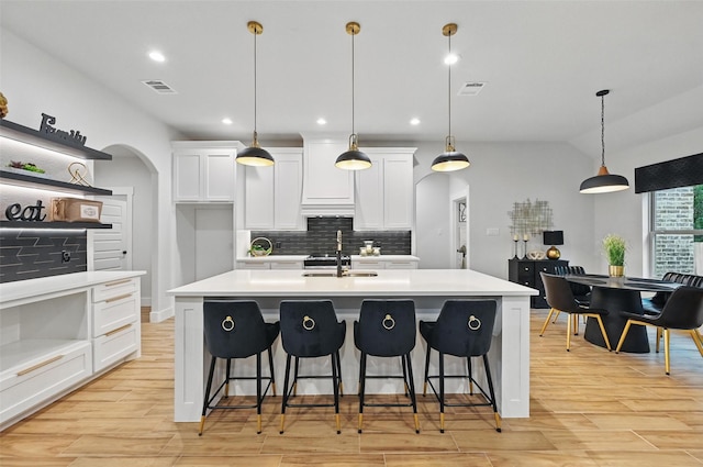 kitchen with a sink, light countertops, arched walkways, white cabinetry, and backsplash