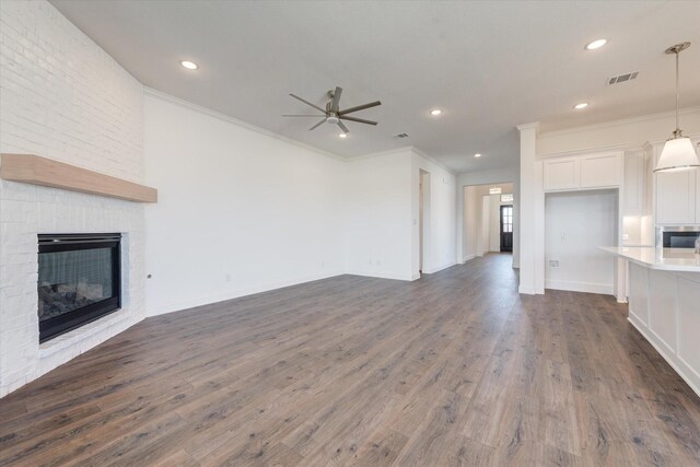 unfurnished living room featuring crown molding, dark wood finished floors, a large fireplace, a ceiling fan, and visible vents