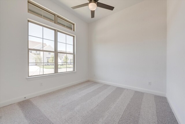 carpeted spare room featuring baseboards and a ceiling fan