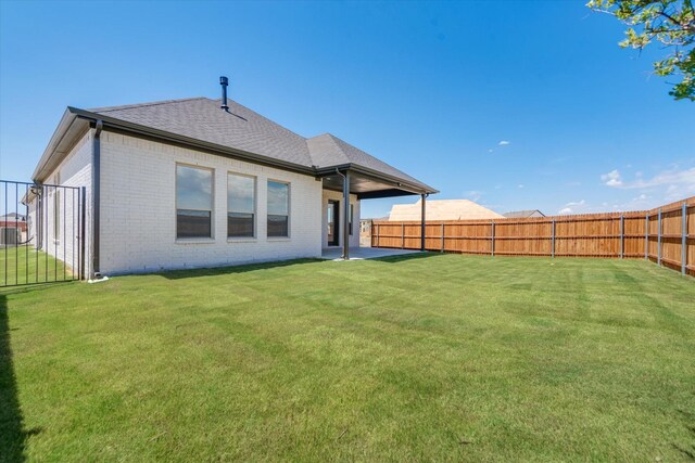 rear view of property featuring a shingled roof, brick siding, a fenced backyard, a patio area, and a yard