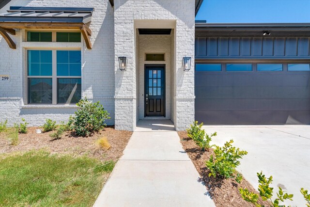 doorway to property with board and batten siding, brick siding, an attached garage, and driveway