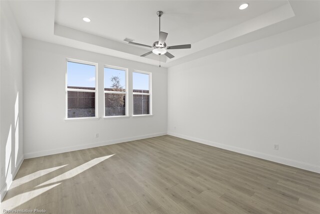 empty room with a ceiling fan, wood finished floors, a raised ceiling, baseboards, and recessed lighting