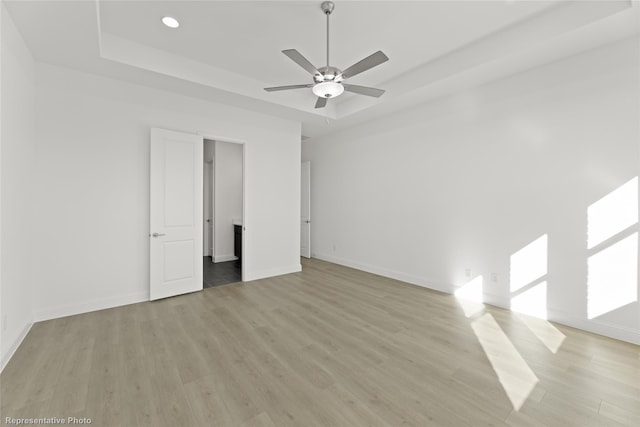 interior space with baseboards, recessed lighting, a tray ceiling, a ceiling fan, and light wood-style flooring