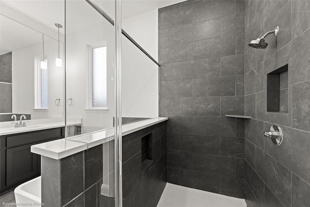 bathroom with a tile shower, a healthy amount of sunlight, and vanity