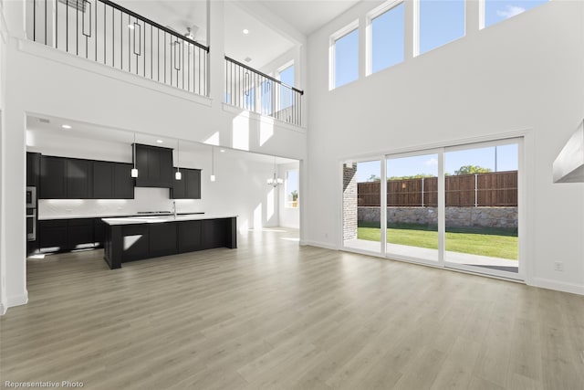 unfurnished living room with light wood-style floors, baseboards, a towering ceiling, and a wealth of natural light