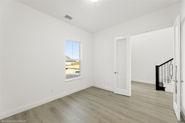 unfurnished room featuring stairway, baseboards, light wood-type flooring, and visible vents