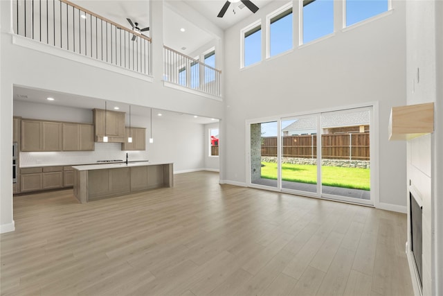 2206 Stratford Rd, Rockwall, TX 75087 - unfurnished living room featuring ceiling fan, a towering ceiling, baseboards, light wood finished floors, and a fireplace