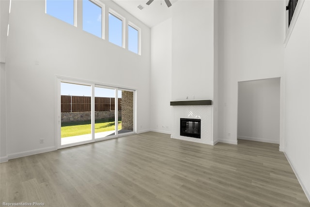 unfurnished living room featuring a fireplace, a ceiling fan, wood finished floors, and a towering ceiling