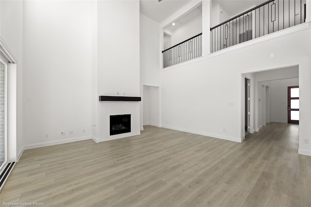 unfurnished living room featuring light wood-style floors, baseboards, a towering ceiling, and a fireplace
