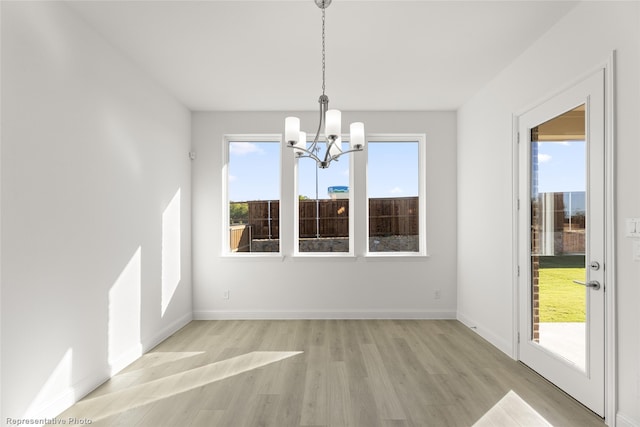 unfurnished dining area with baseboards, light wood-style flooring, and a chandelier