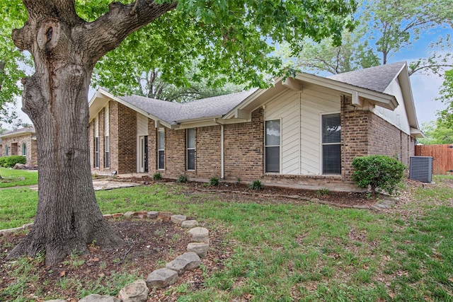 ranch-style home featuring brick siding, fence, a shingled roof, and a front lawn
