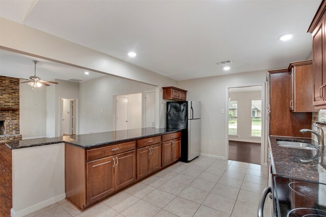 kitchen with ceiling fan, a sink, freestanding refrigerator, dark stone countertops, and light tile patterned flooring