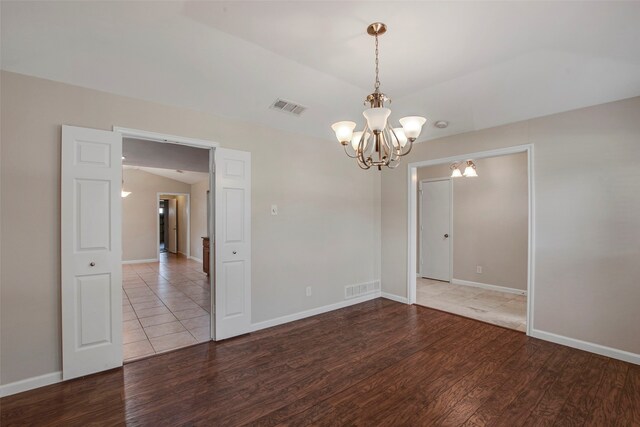 unfurnished room featuring visible vents, wood finished floors, and a notable chandelier
