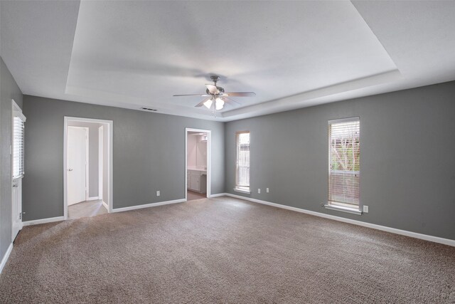 carpeted empty room featuring baseboards, a ceiling fan, a raised ceiling, and plenty of natural light