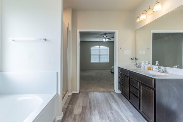ensuite bathroom featuring a garden tub, a sink, ceiling fan, and wood finished floors