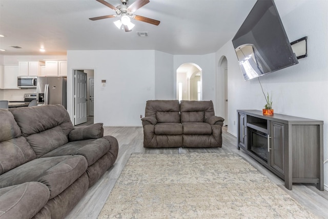 living room with light wood-style floors, arched walkways, a ceiling fan, and visible vents