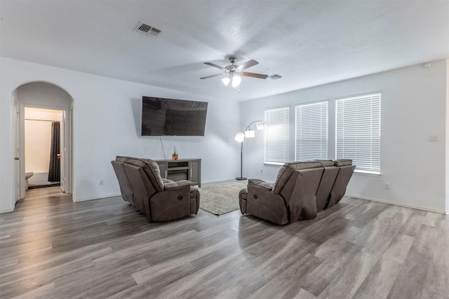living area featuring visible vents, a ceiling fan, wood finished floors, a fireplace, and arched walkways