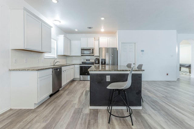 kitchen with light wood-style floors, a center island, arched walkways, a sink, and stainless steel appliances