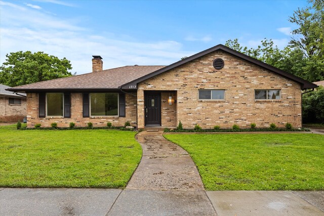view of front of house with brick siding, a chimney, a front yard, and a shingled roof