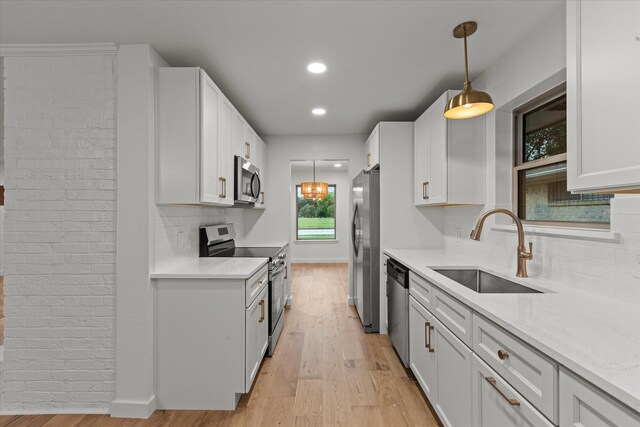 kitchen with stainless steel appliances, a sink, light wood-style floors, backsplash, and decorative light fixtures