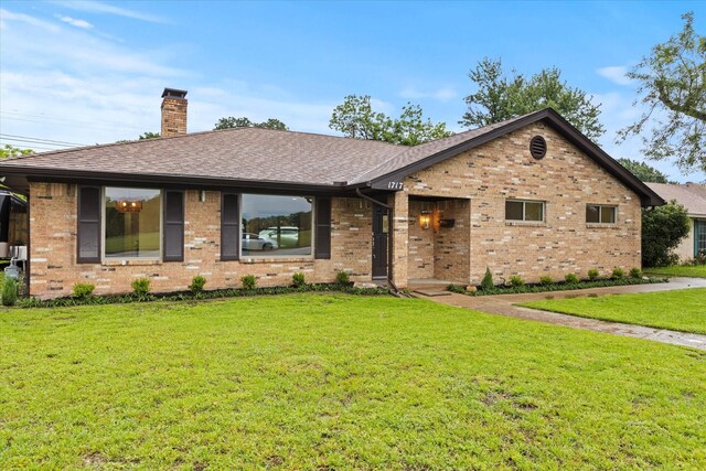 ranch-style home featuring brick siding, a front yard, a chimney, and roof with shingles